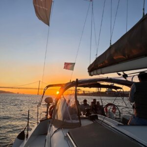Clients enjoying a sunset river cruise on the Tagus River in Lisbon with the 25 de Abril Bridge in the background.