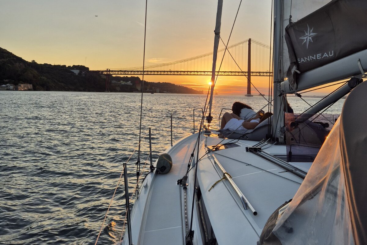 Clients relaxing on a private boat during sunset on the Tagus River with the 25 de Abril Bridge in the background.