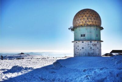 View from the Torre da Serra da Estrela covered in snow, with a clear sky and mountainous landscape in the background, during winter in Portugal.