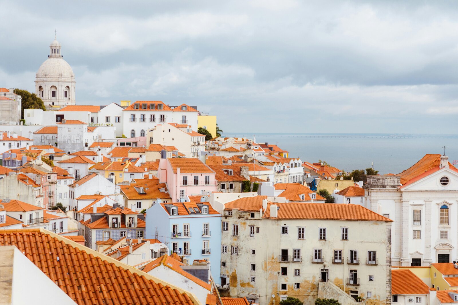 View over the colorful rooftops of the Alfama neighborhood in Lisbon, highlighting the National Pantheon and the Tagus River in the background, an iconic stop in the cultural tours of Premium Tours.