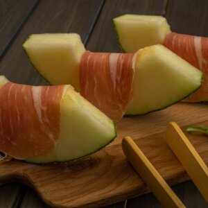 Fresh melon slices wrapped in Portuguese cured ham served on a wooden board.