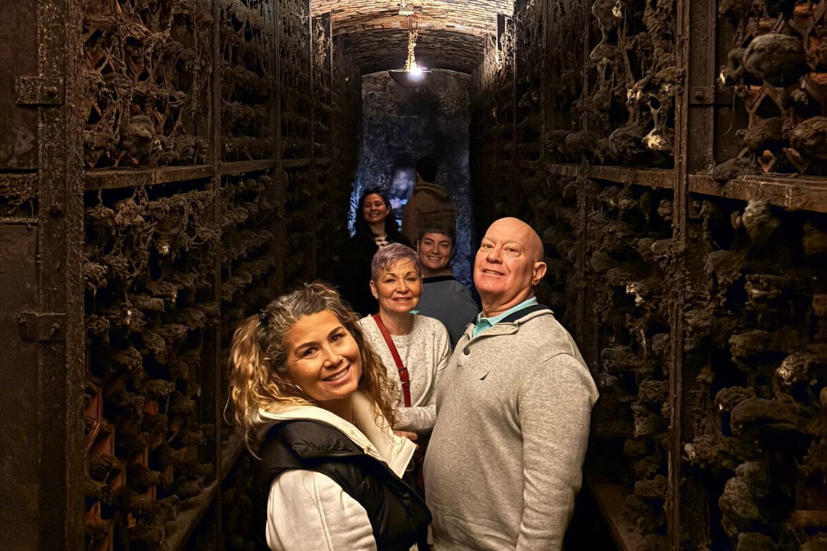 Visitors walking through a historic Port wine cellar lined with aging wine barrels in Porto, Portugal.