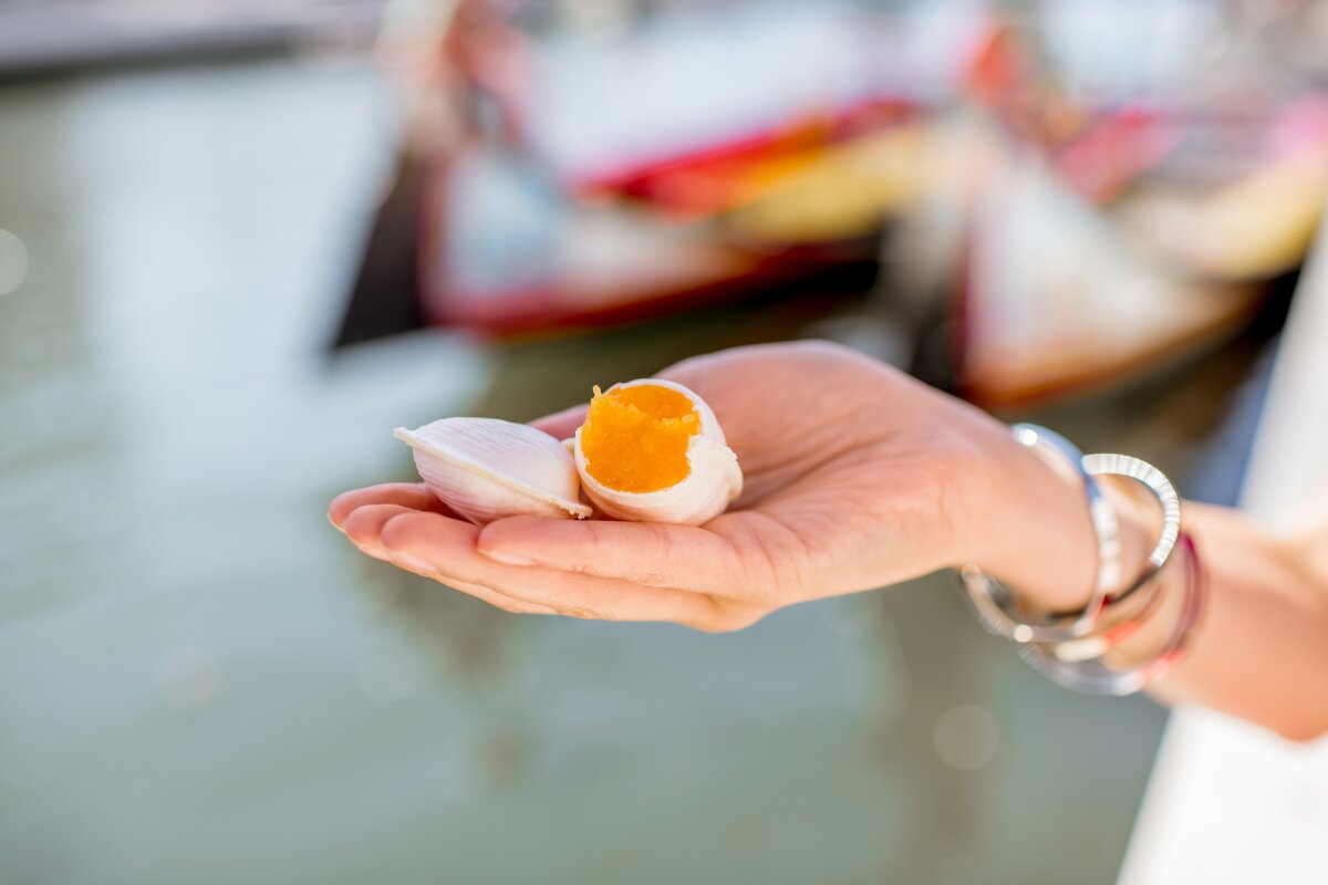 Traditional Ovos Moles de Aveiro in a delicate shell-shaped wafer, held in a person's hand by the waterfront.