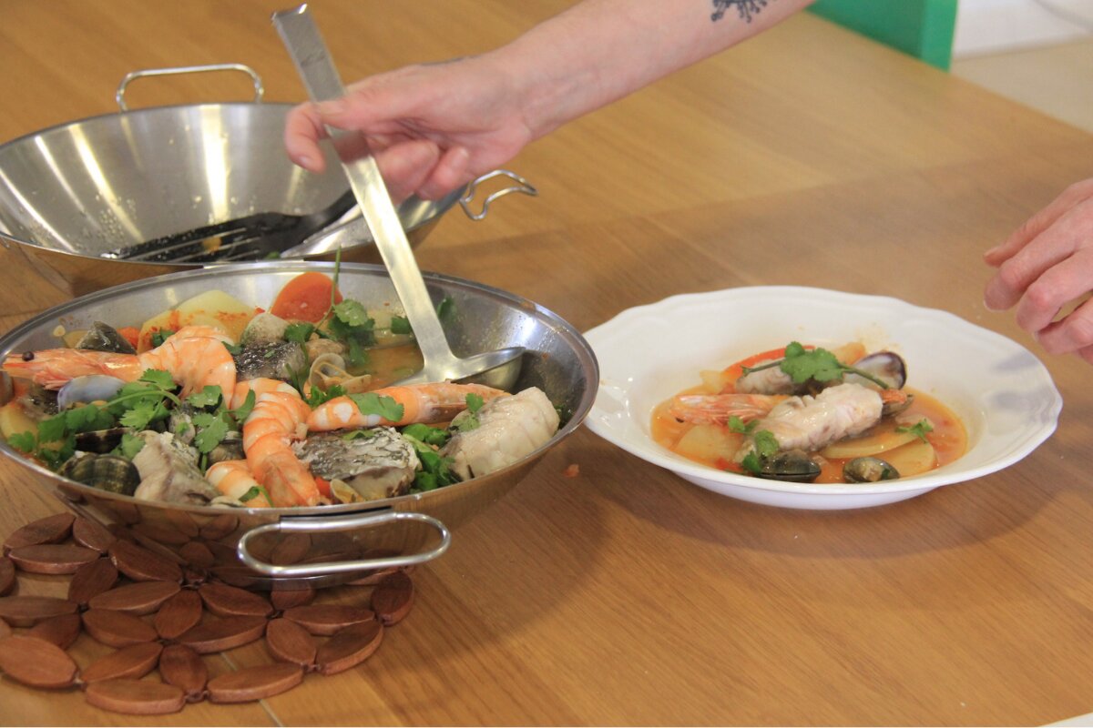 Traditional Portuguese seafood cataplana with prawns, fish, clams, potatoes, and fresh coriander being served into a bowl.